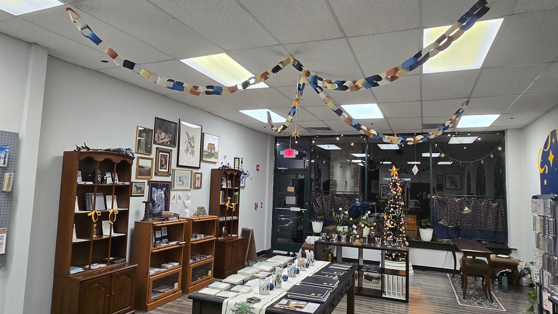 a Christmas tree decorated with gold and blue ornaments at the indoor window of a stationery shop filled with displays of notebooks, stickers, and pens